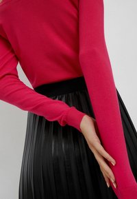 Maglione rosa aderente a maglia con maniche lunghe, abbinato a una gonna nera plissettata in ecopelle con vita elasticizzata.