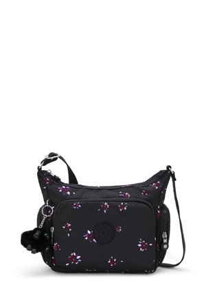 Black fabric shoulder bag with floral print, featuring a circular logo, zippered pockets, and a furry pom-pom keychain. Adjustable strap.