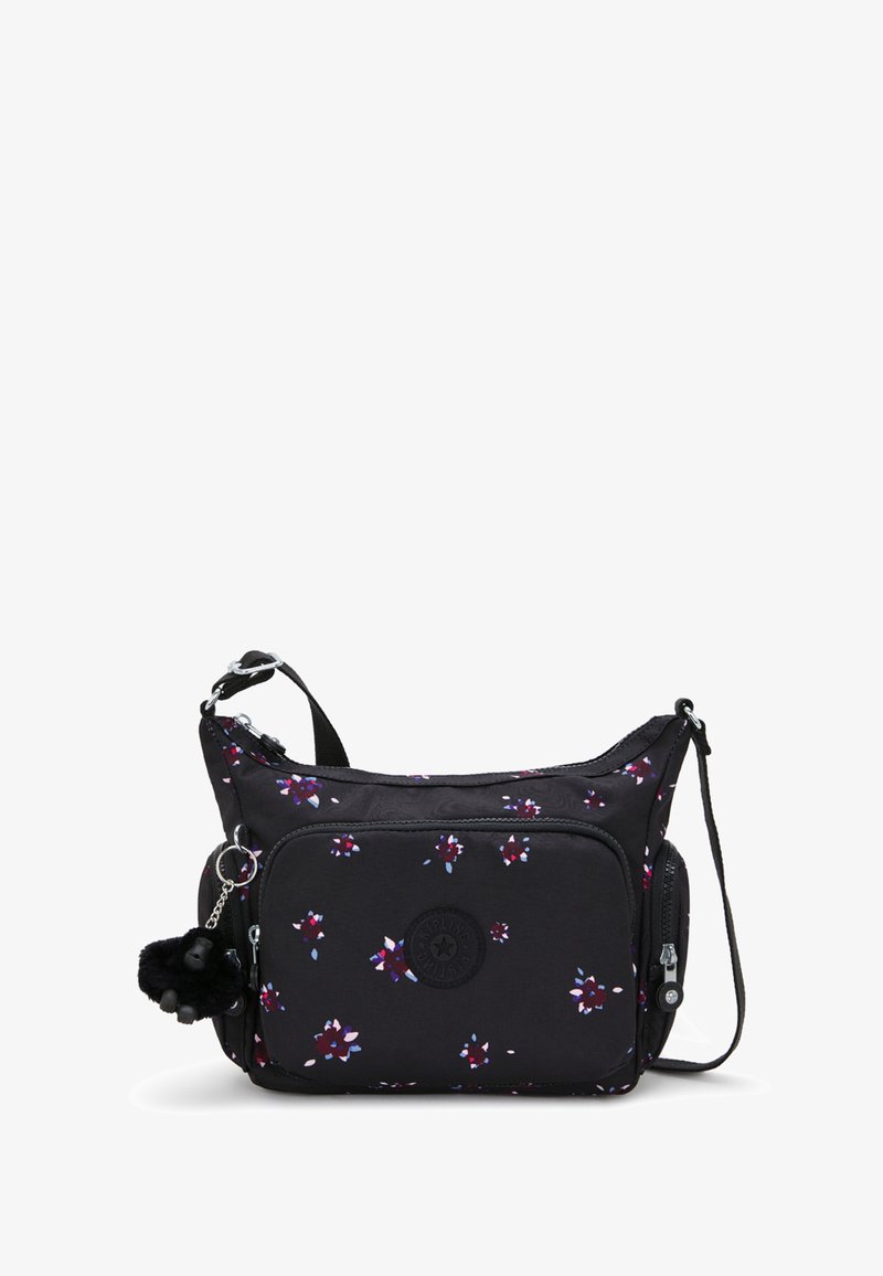 Svart tygaxelväska med blommigt mönster, försedd med en cirkulär logotyp, dragkedjefickor och en plyschpom-pom nyckelring. Justerbar rem.