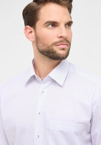 Camicia bianca con un motivo a griglia lilla chiaro, colletto button-down e piccoli bottoni argentati. Il tessuto appare liscio con una vestibilità su misura.