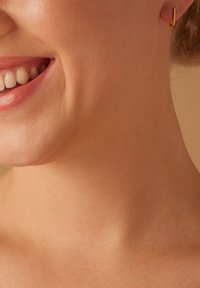 Gouden hoepeloorbel in een minimaal ontwerp, met een gebogen vorm. Close-up van de oorbel tegen een gladde huid, waarbij de textuur wordt benadrukt.