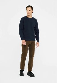 Tumši zils džemperis ar apaļu kaklu mīkstā audumā, kombinēts ar brūnām šinzonbiksēm un melniem apaviem, ar pieguļošu piegriezumu un ribaina auduma aprocēm.