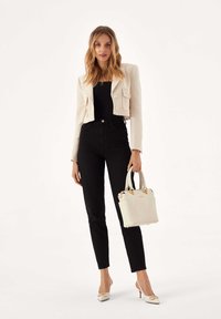 Krótka, w paski marynarka w kremowym kolorze z dwoma przednimi kieszeniami, zestawiona z wysokim stanem czarnymi dżinsami. Trzyma białą torebkę ze złotymi zdobieniami.