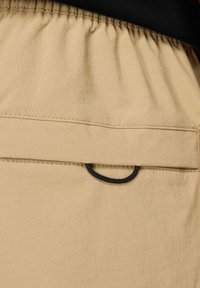 Beżowe bawełniane szorty z elastycznym pasem, tylną kieszenią z czarną pętlą do zabezpieczania przedmiotów oraz gładką fakturą.