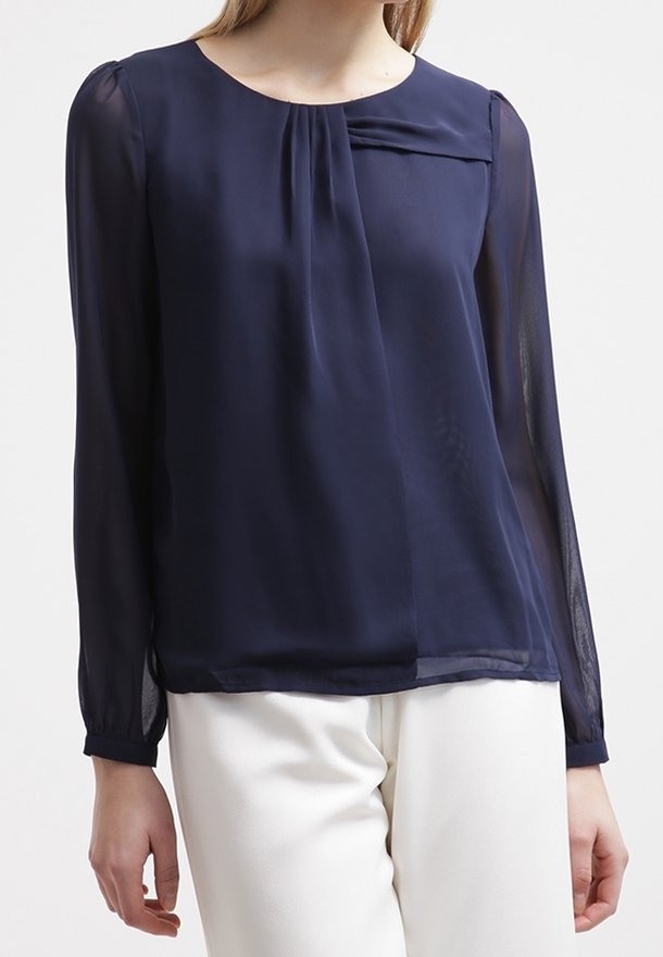 Marineblaue Bluse mit langen Ärmeln aus durchscheinendem Stoff, mit rundem Halsausschnitt und dezenten Faltendetails in der Brustpartie. Sanfte Textur.