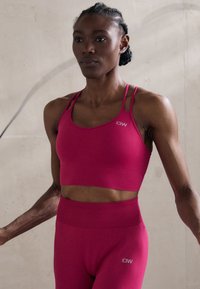 Rozi sportski crop top i tajice viskog struka s rebrastom teksturom. Top ima tanke naramenice i logo na grudima.