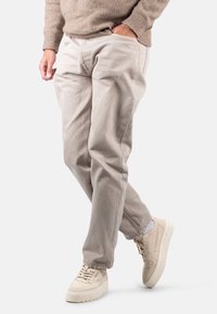 Helle beige Baumwoll-Chinos mit einer lockeren Passform, seitlichen Taschen und einem schmal zulaufenden Bein. Kombiniert mit cremefarbenen Sneakers.