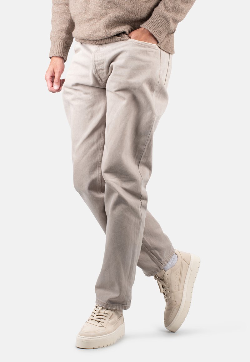 Helle beige Baumwoll-Chinos mit einer lockeren Passform, seitlichen Taschen und einem schmal zulaufenden Bein. Kombiniert mit cremefarbenen Sneakers.