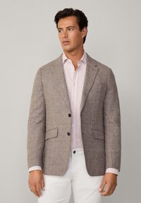 Blazer marron à carreaux en tissu texturé, doté de deux poches avant et de boutons noirs, porté par-dessus une chemise rayée rose clair.