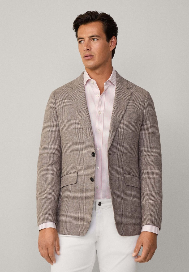 Blazer marron à carreaux en tissu texturé, doté de deux poches avant et de boutons noirs, porté par-dessus une chemise rayée rose clair.