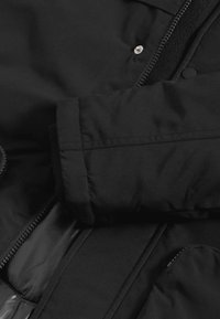 Czarna ocieplana kurtka o teksturowanej powierzchni, z zatrzaskami i kieszenią zapinaną na zamek; posiada ściągacze na mankietach oraz gładką podszewkę.