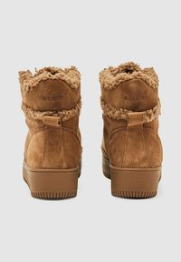 Brune ruskindsankle støvler med en blød krave, struktureret detalje og en solid gummisål. Forstærket hæl og præget logo bagpå.