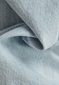 Lichtblau denimstof met een zachte, gestructureerde oppervlakte, gekenmerkt door zichtbare diagonale weefpatronen en een gladde afwerking.