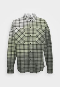 Camicia a quadri in tonalità di verde e nero, con colletto button-down e due tasche sul petto con distinti motivi diagonali. Orlo sfilacciato.