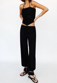 Haut noir sans manches avec un décolleté droit et un pantalon ample assorti, doté d'une taille à cordon et de liens décoratifs aux chevilles.
