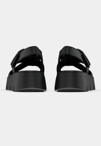 Black platform sandals with wide straps and a rectangular buckle, featuring a textured sole and a flat, contoured base for stability.