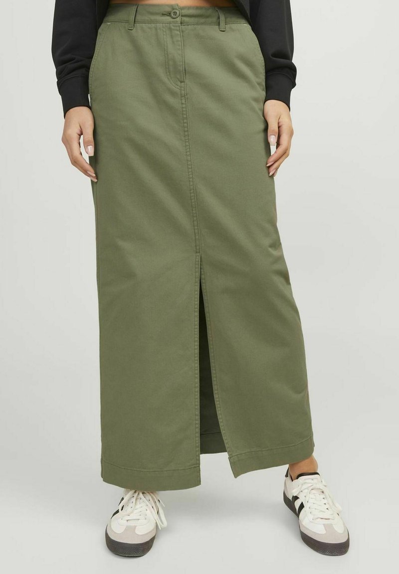 Falda larga de mezclilla verde oliva con abertura frontal, cierre de botón y cremallera, y presillas para cinturón. Combinada con zapatillas blancas y negras.