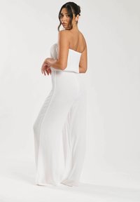 Mono blanco sin tirantes con una textura acanalada, diseño de pierna ancha y corsé ajustado, que muestra una silueta suave y un estilo minimalista.
