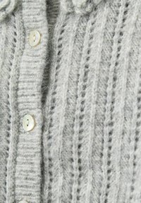 Harmaa neulecardigan, jossa on ribbikuvio ja suuret vaaleat napit. Kangas näyttää pehmeältä ja mukavalta.