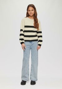 Un pull surdimensionné crème avec des rayures noires horizontales, associé à un jean large bleu clair et des chaussures noires épaisses. Texture en maille lisse.