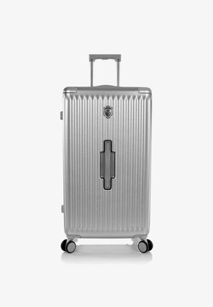 Valise rigide argentée avec des nervures verticales, une poignée télescopique, quatre roues pivotantes et une poignée latérale encastrée centrée.