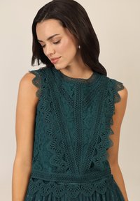 Türkises Spitzenkleid mit gewellten Kanten, aufwendigen Blumenmustern und einem strukturierten Oberteil. Verfügt über eine taillierte Taille und einen geschichteten Rock.