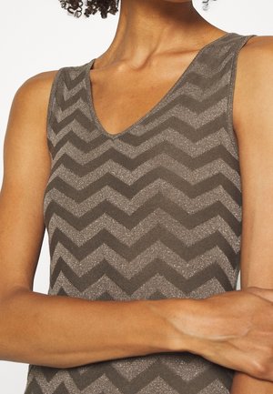 Personne portant un haut sans manches avec un motif chevron marron et gris, col en V, bras croisés, montrant le haut du torse et le cou.