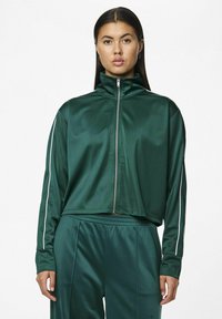 Grøn, lynlåset træningsjakke med høj krave, lavet af glat materiale, med hvide sidestriber og et cropped design.