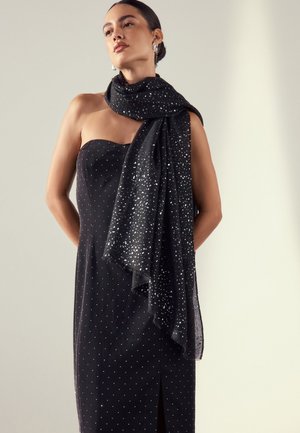 Schwarzer Schal mit silbernem Punktmuster, drapiert über ein trägerloses schwarzes Kleid mit Schlitz und subtilen Details. Weicher, strukturierter Stoff.