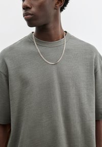 Grå kortærmet t-shirt med rund halsudskæring i tekstureret stof og en afslappet pasform, sat sammen med et sølvfarvet kæderegul.