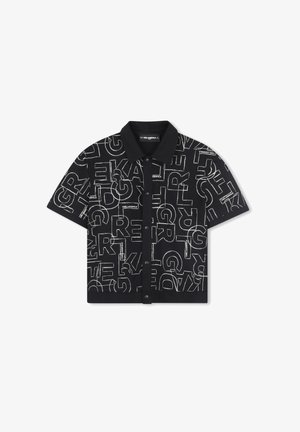 Chemise noire à manches courtes avec col, présentant un motif de texte répété en blanc audacieux. Le tissu semble lisse avec une coupe structurée.