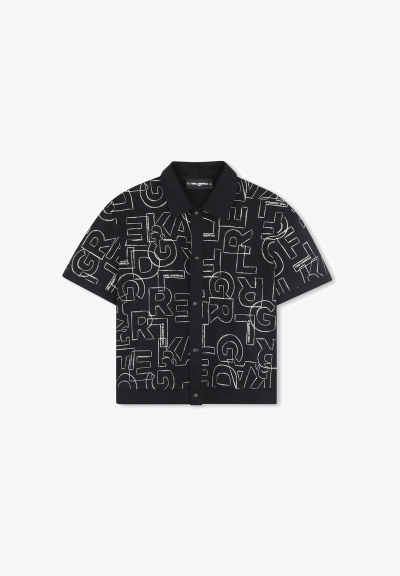 Chemise noire à manches courtes avec col, présentant un motif de texte répété en blanc audacieux. Le tissu semble lisse avec une coupe structurée.