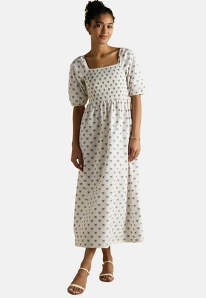 Weißes Kleid mit blauem Blumenmuster, quadratischem Ausschnitt, kurzen Puffärmel und gestuften Oberteil. Fließende Maxi-Länge mit lockerer Passform.