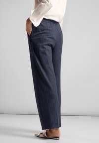 Pantalons rayés bleu marine à coupe droite, dotés de poches latérales et d'une texture lisse. Accompagnés de chaussures à enfiler métalliques.