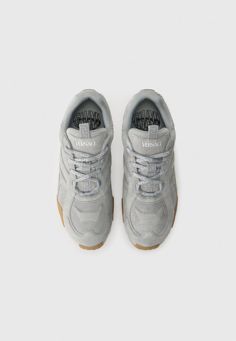 Grijze suède sneakers met lichtgrijze veters, met een gestructureerde bovenkant, "VERSACE" branding en een gumrubberen zool.