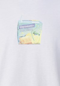 Valkoinen t-paita, jossa on pieni grafiikka sinivalkoisesta ja keltaisesta mehukartongista, jossa on pillin kuva, sekä paahto- ja sitruunakuviot.