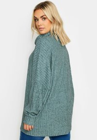 Teal neulepaita, jossa on ribbaustekstuuri, korkea kaulus ja pitkät hihat. Löysähkö malli, joka ulottuu lantion yli. Pehmeää materiaalia.