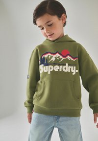 Olivově zelená mikina s kapucí a přední kapsou, s grafikou hory a slunce v červené, bílé a modré barvě a logem "Superdry." na hrudi.