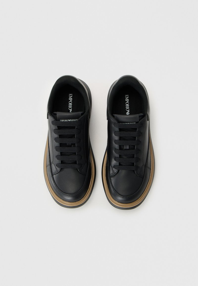 Zapatillas negras de cuero con textura suave, punta redonda y seis ojetes. Presenta una suela de goma color caramelo y un logo en la lengüeta.