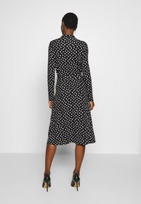 Svart långärmad klänning med ett vitt abstrakt mönster, knälång kjol och en figursydd midja. Bärs med svarta högklackade skor.