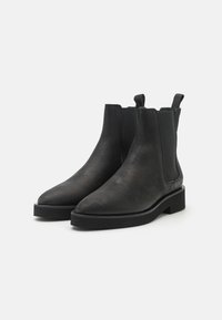 Mustad nahast ankle kingad, millel on sile tekstuur, terav nina ja elastsed külgpaneelid. Omab paksu, triibulist kummitalda.