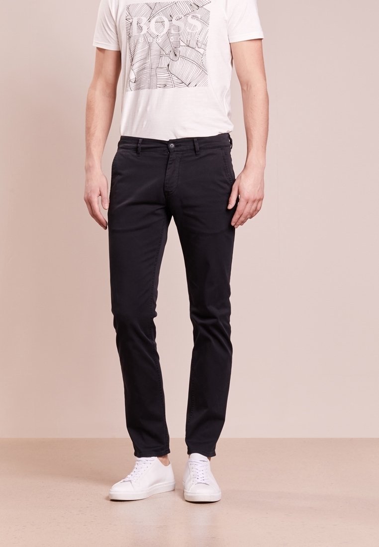 Pantalon en coton noir à coupe slim, devant plat, cinq poches et taille mi-haute, associé à un t-shirt blanc à motif graphique et des baskets blanches.