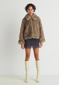 Faux fur-jakke i brun med krage, med vide ermer og en avslappet passform, kombinert med et rutemønstret miniskjørt og knelange hvite støvler.