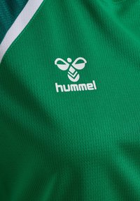 Tissu de sport vert avec logo hummel blanc représentant une abeille stylisée et une bande blanche et bleu marine près du bord.