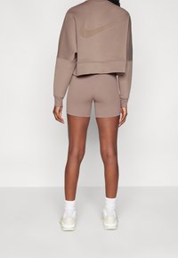 Persona che indossa un felpa corta color malva e pantaloni corti abbinati con un grande logo Nike sulla schiena, calzini bianchi e scarpe da ginnastica bianche, in piedi di spalle.