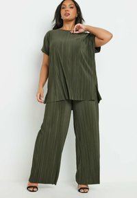 Olivgrön plisserad set som består av en lös topp med korta ärmar och vida byxor. Tyget har en slät, texturerad yta och sidofack.