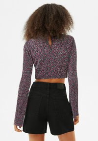 Haut court à manches longues dans un imprimé floral avec des accents roses et violets, associé à un short en denim noir taille haute avec des poches à rabat.