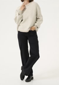 Person wearing beige striped knit sweater, black wide-leg pants, and black chunky loafers, standing with one hand in pocket.