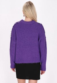 Lila gestrickter Pullover mit lockerem Schnitt, aus strukturiertem Stoff, mit geripptem Saum und dekorativen metallischen Akzenten an den Schultern.