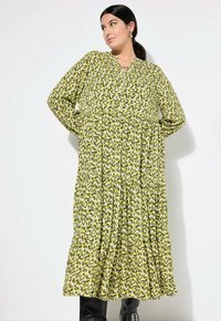 Vestido maxi estampado en verde con escote en V, mangas largas, botones y dobladillo en capas. La tela presenta un patrón similar a hojas en tonos de verde.
